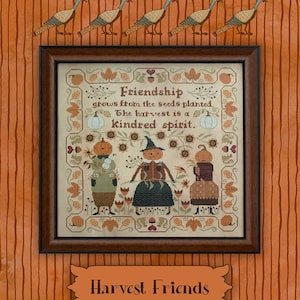 Peut inclure: Un échantillon de point de croix encadré représentant trois personnages à tête de citrouille dans un jardin, entourés d'une bordure de feuilles, de glands et d'écureuils. Le texte indique : Friendship grows from the seeds planted. The harvest is a kindred spirit. Harvest Friends.