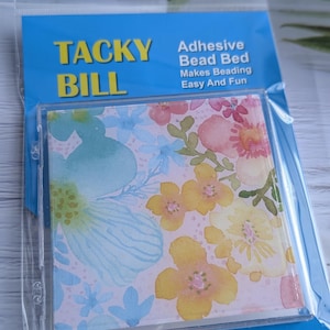 May include: A package for an adhesive bead bed, with the text "TACKY BILL" in yellow and blue. The bead bed features a floral design with watercolor flowers in pink, yellow, and blue. The text "Makes Beading Easy And Fun" is also visible.