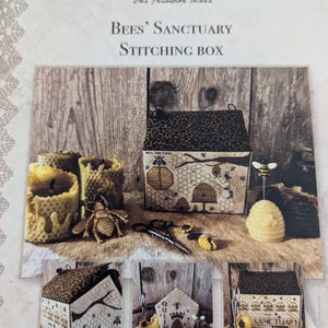 May include: A stitching box kit with a bee theme. The box is shaped like a house and has a beehive design. The kit includes fabric, thread, needles, and instructions. The box is decorated with bees, flowers, and a honeycomb.