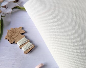 May include: White Aida cloth for cross stitch, with a wooden thread holder, pink embroidery scissors, and a pink tassel.
