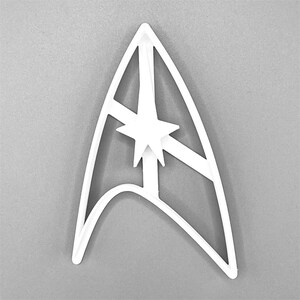 Puede incluir: Cortador de galletas de pl&aacute;stico blanco con forma del emblema de la Flota Estelar de Star Trek. El emblema presenta una estrella estilizada en el centro.