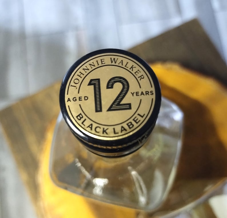 May include: A clear glass bottle with a black and gold cap. The cap reads "JOHNNIE WALKER" and "BLACK LABEL 12 YEARS AGED". The bottle's square shape is partially visible.