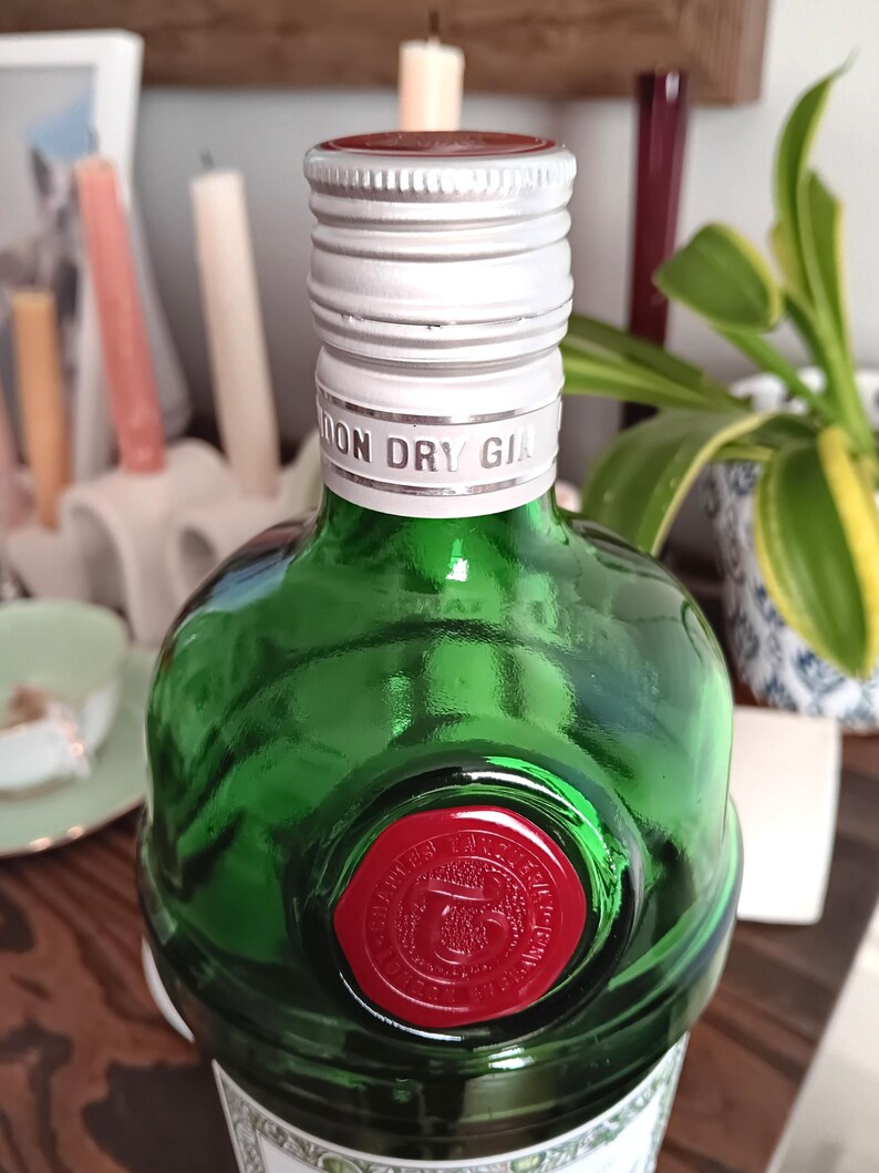 May include: A green glass bottle of London Dry Gin with a silver cap and a red wax seal. The bottle has a rounded shape and the words "LONDON DRY GIN" are printed on the cap. The seal features an emblem and text.
