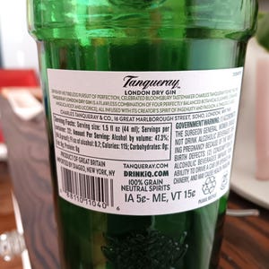 May include: A green glass bottle of Tanqueray London Dry Gin. The label includes text about the gin's ingredients and origin. The bottle has a barcode and a recycling symbol. The bottle contains 1.5 fl oz (44 ml) of gin.