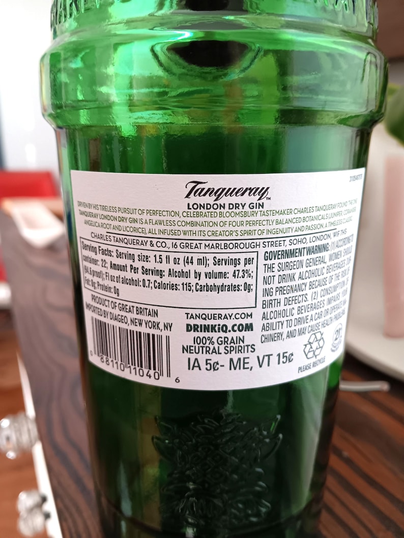May include: A green glass bottle of Tanqueray London Dry Gin. The label includes text about the gin's ingredients and origin. The bottle has a barcode and a recycling symbol. The bottle contains 1.5 fl oz (44 ml) of gin.