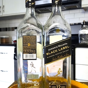 May include: Two empty Johnnie Walker Black Label blended scotch whisky bottles. The bottles are clear with black and gold labels. The labels include the text "Johnnie Walker Black Label" and "Aged 12 Years".