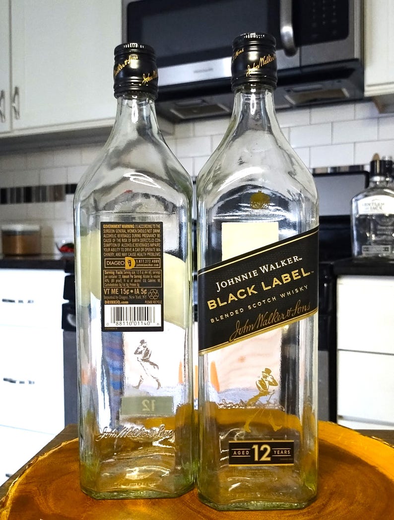 May include: Two empty Johnnie Walker Black Label blended scotch whisky bottles. The bottles are clear with black and gold labels. The labels include the text "Johnnie Walker Black Label" and "Aged 12 Years".