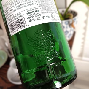 May include: A green glass bottle of Tanqueray London Dry Gin. The bottle has a pineapple emblem embossed on the glass. The label includes text about the product, including alcohol content and serving size. The bottle is partially visible.