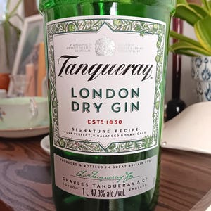 May include: A green glass bottle of Tanqueray London Dry Gin. The label features the brand name, product details, and the text "ESTD 1830". The bottle contains 1 liter of gin with 47.3% alcohol by volume.