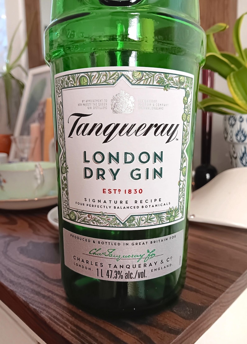 May include: A green glass bottle of Tanqueray London Dry Gin. The label features the brand name, product details, and the text "ESTD 1830". The bottle contains 1 liter of gin with 47.3% alcohol by volume.