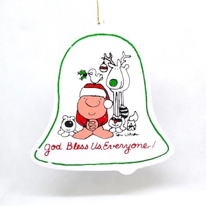 May include: White ceramic Christmas ornament shaped like a bell with a green outline. The ornament features a cartoon illustration of a person in a Santa hat with a reindeer, a bird, and two dogs. The text "God Bless Us, Everyone!" is written on the ornament.