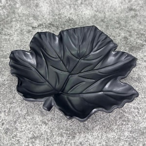 May include: A black ceramic dish shaped like a leaf. The dish features a detailed leaf design and a smooth, glossy finish.