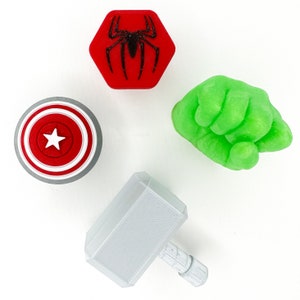 May include: A set of five 3D printed figurines. The figurines are a red spider, a green fist, a grey hammer, and two round figures with a red star and a white star.