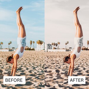 May include: A woman in a white tank top and denim shorts does a handstand on a sandy beach. The sky is blue and there are palm trees in the background.