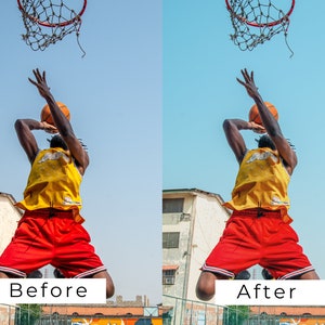 Op de afbeelding: Een basketballer in een geel shirt en rode broek springt om een basketbal door een ring te gooien. De speler is in de lucht met de bal in zijn hand. De lucht is blauw en er is een gebouw op de achtergrond.