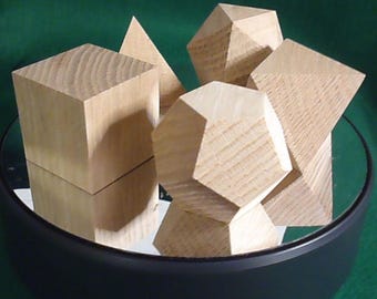 Op de afbeelding: Vijf geometrische vormen van hout, waaronder een kubus, een piramide, een dodecaëder, een icosaëder en een hexaëder, zijn gerangschikt op een zwart rond platform.