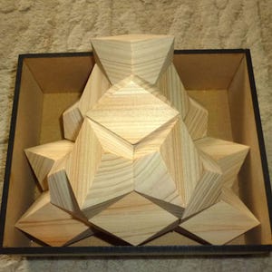 Peut inclure: Un puzzle géométrique en bois composé de pièces triangulaires et en forme de losange qui s'emboîtent. Le puzzle est présenté dans une boîte marron clair bordée de noir. Le grain naturel du bois est visible sur les pièces.