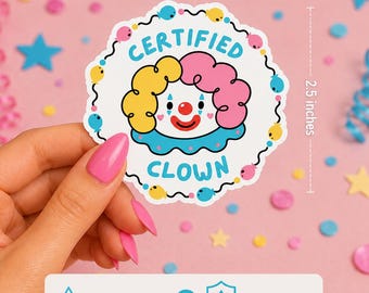 May include: A circular sticker featuring a clown face with yellow and pink hair, a red nose, and blue accents. The text CERTIFIED CLOWN is printed in blue. The sticker measures 2.6 inches in width and 2.5 inches in height, with a border of small balloons.