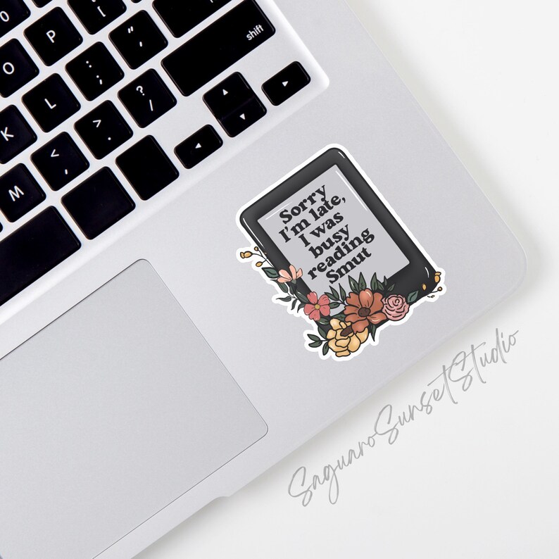 May include: A sticker of a black and white e-reader with the text "Sorry I'm late, I was busy reading Smut". The e-reader is surrounded by colorful flowers.