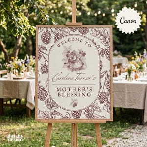 Puede incluir: Un letrero de bienvenida rectangular sobre un caballete de madera con una ilustración botánica de color rojo oscuro de moras y hojas. El óvalo central contiene el texto Welcome to Caroline Turner's Mother's Blessing y un conejo.