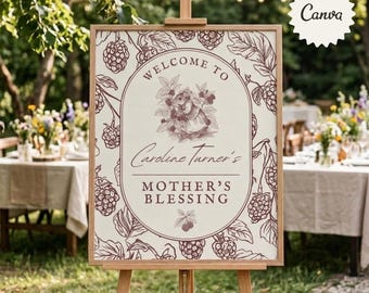 May include: A rectangular welcome sign on a wooden easel featuring a dark red botanical illustration of blackberries and leaves. The center oval contains the text Welcome to Caroline Turner's Mother's Blessing with a small illustration of a rabbit.