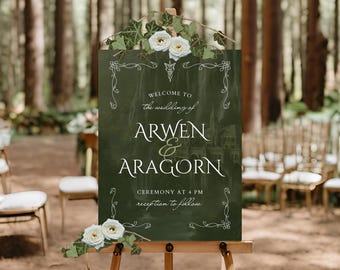 Puede incluir: Un cartel de boda verde con flores blancas y hiedra. El cartel dice "Bienvenido a la boda de Arwen & Aragorn. Ceremonia a las 4 PM, recepción a continuación."