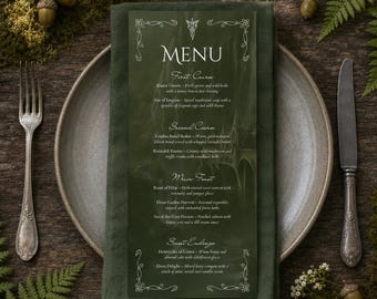 May include: A dark green rectangular menu card with white text and ornate border detailing, placed on a folded dark green linen napkin and a gray ceramic plate. A silver fork and knife are positioned on either side of the plate.