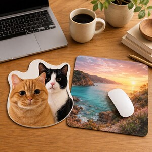 May include: A wooden desk with two mouse mats and a computer mouse. One mouse mat is cat-shaped, featuring a ginger and a black and white cat. The other shows a coastal sunset scene.