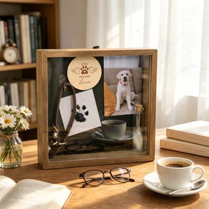 Könnte beinhalten: Ein Holzschattenkasten mit Glasfront zeigt ein Foto eines Welpen, einen Pfotenabdruck und eine Holzscheibe mit dem Namen "Luna". Ein Hundehalsband, eine Tasse Kaffee und eine Brille sind ebenfalls zu sehen.