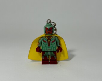 Puede incluir: Una minifigura Lego verde y roja de Vision de los Vengadores de Marvel, que lleva una capa amarilla y una pieza de pecho roja y dorada. La minifigura tiene un llavero unido a la parte superior de su cabeza.