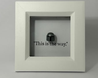 May include: A white picture frame with a gray Mandalorian helmet figurine and the text "This is the way." inside.