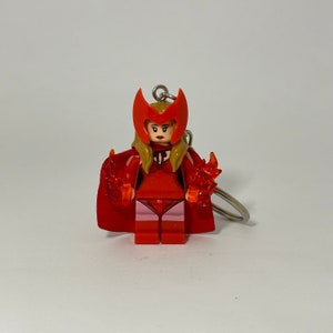 May include: Red and pink Lego minifigure of Scarlet Witch with a red cape and fire effects in her hands. The minifigure is attached to a silver keychain.