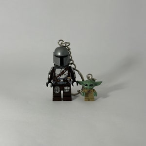 Peut inclure: Un porte-clés argenté avec une figurine Lego de The Mandalorian portant une combinaison marron et argent et une figurine Lego de Grogu verte et marron.