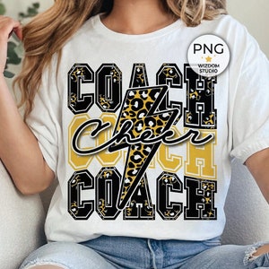 May include: A white t-shirt with a black and gold graphic that says "Coach Cheer Coach" with a leopard print and lightning bolt design.