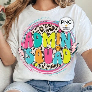 May include: White t-shirt with a colorful "ADMIN SQUAD" graphic. The design features a leopard print circle, a smiley face, and a lightning bolt. The shirt is worn with light blue jeans.