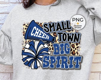 Peut inclure: Un sweat-shirt gris clair avec un motif de pom-pom girl bleu et blanc. Le motif comprend un mégaphone, des pompons et les mots "Small Town Big Spirit". Le sweat-shirt a des manches longues.