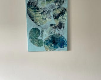 May include: Abstract art piece featuring organic shapes in shades of blue, green, and white on a light blue background. The artwork is mounted on a rectangular canvas and hangs on a white wall. The painting's composition is reminiscent of aquatic forms.