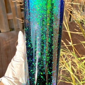 Pu&ograve; includere: Un bicchiere alto e trasparente con un design di glitter nero e verde. Il glitter &egrave; iridescente e crea un effetto sfumato dal verde scuro al nero.