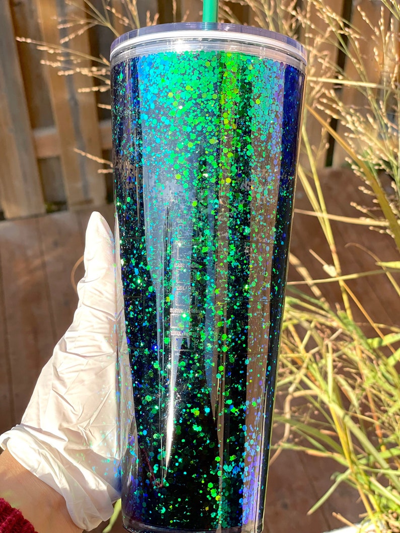 Pu&ograve; includere: Un bicchiere alto e trasparente con un design di glitter nero e verde. Il glitter &egrave; iridescente e crea un effetto sfumato dal verde scuro al nero.