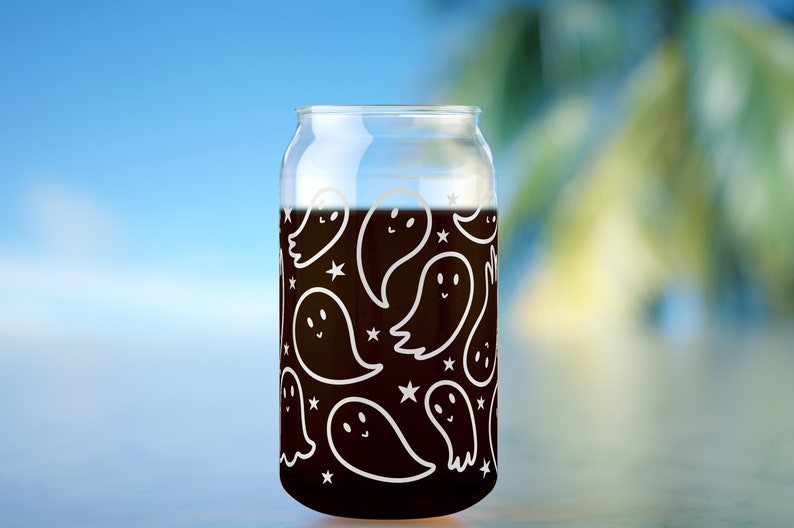 May include: A clear glass can with a black liquid inside. The can is decorated with a white pattern of ghosts and stars.