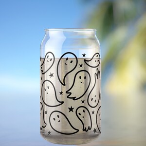 May include: A clear glass can with a black and white ghost pattern. The ghosts have smiling faces and are surrounded by stars.
