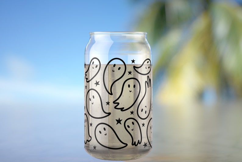 May include: A clear glass can with a black and white ghost pattern. The ghosts have smiling faces and are surrounded by stars.