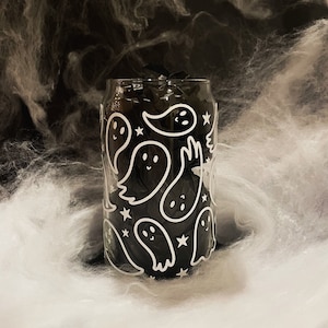 May include: A clear glass can with a black and white ghost pattern. The ghosts are outlined in white and have a black interior. The can is filled with black tissue paper.