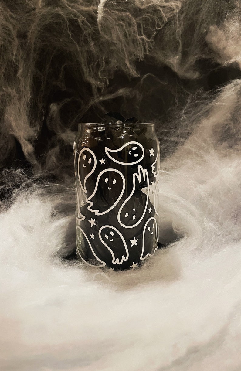 May include: A clear glass can with a black and white ghost pattern. The ghosts are outlined in white and have a black interior. The can is filled with black tissue paper.