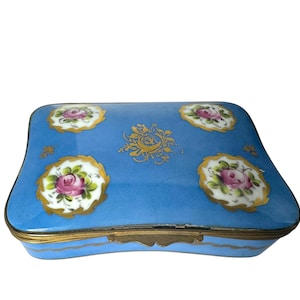 May include: A blue porcelain trinket box with a hinged lid. The box is decorated with gold trim and floral designs in shades of pink, white, and green.
