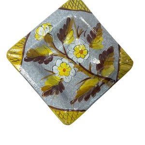 May include: A square ceramic dish with a gray glaze and a yellow and brown floral design. The dish has a yellow border with a woven pattern.