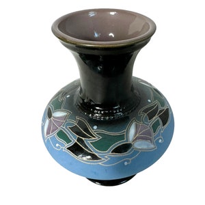 May include: A ceramic vase with a bulbous base and a slender neck. The vase features a black body with a light blue base and a brown interior. Floral designs in white, green, and purple adorn the vase, adding a decorative touch.