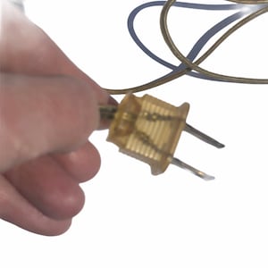 Puede incluir: Primer plano de un enchufe el&eacute;ctrico dorado con dos clavijas. El enchufe est&aacute; conectado a un cable el&eacute;ctrico marr&oacute;n.