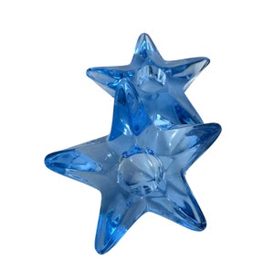 May include: A set of two blue glass star-shaped candle holders. The holders are stacked on top of each other.