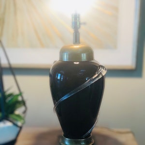 Puede incluir: Una l&aacute;mpara de mesa negra y dorada con un dise&ntilde;o de vidrio transparente. La l&aacute;mpara tiene una base redonda y una pantalla de vidrio transparente.